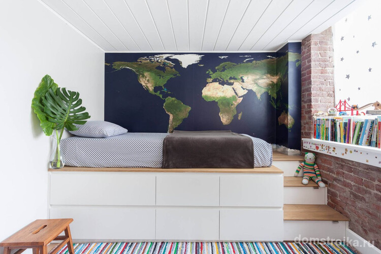 Стильная комната для мальчика с картой мира на одной из стен вместо обоев и кроватью на подиуме