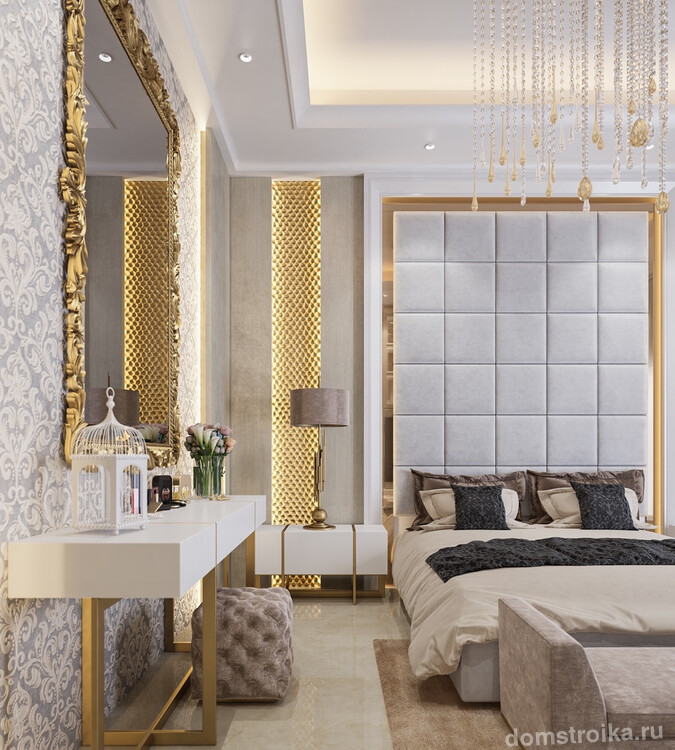 Спальня класса люкс с нотами декадентства в декоре. Высокое изголовье обито искусственной замшей, а массивная позолоченная рама зеркала перекликается с подсвеченными золотистыми вставками на стене