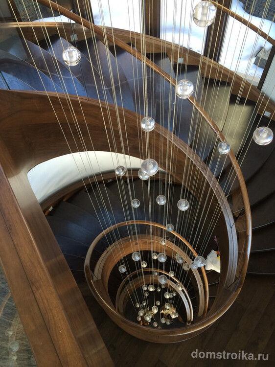 Спиральную деревянную лестницу можно украсить при помощи инсталляции в виде декоративных нитей с бусинами, свисающими по всей высоте лестницы