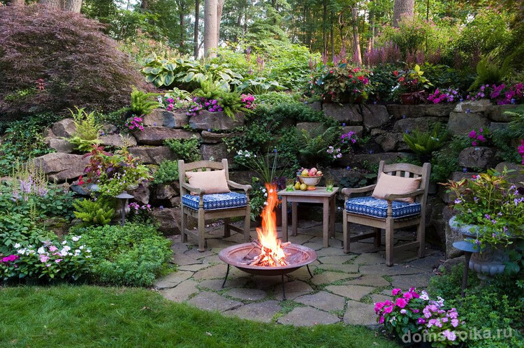 Уютное патио в саду с красивым ландшафтным дизайном и обилием цветущих растений