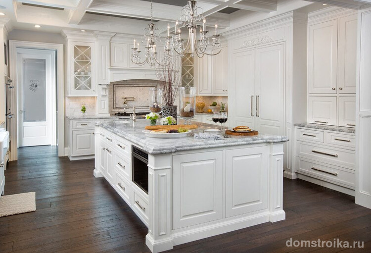 Классическая белая кухня с двумя традиционными люстрами над обеденной областью и точечными светильниками, встроенными в потолок