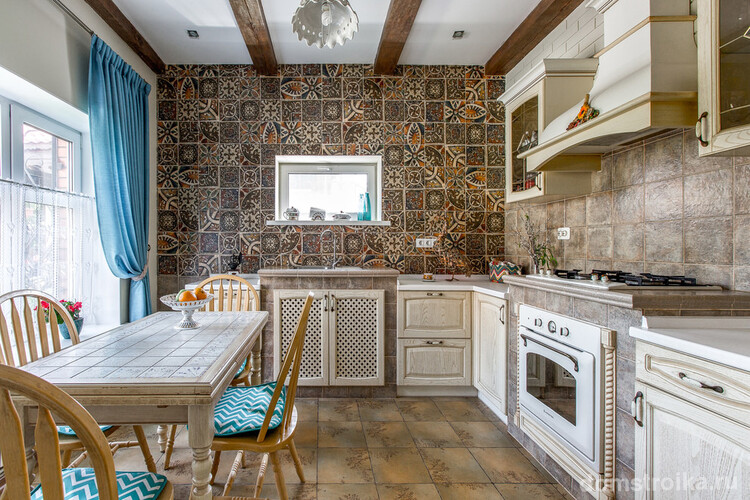 Ярко-голубые шторы в цвет седушек на стульях и мозаичный кафель с рисунком на стене в кухне стиля кантри