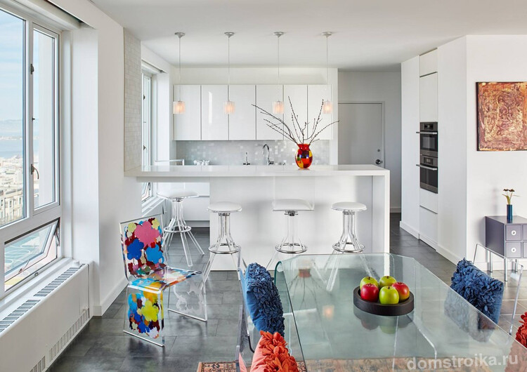 Неординарная белая кухня-студия в небольшой квартире. Яркие акценты на необычных дизайнерских стульях и мелких элементах декора интерьера выглядят очень оригинально