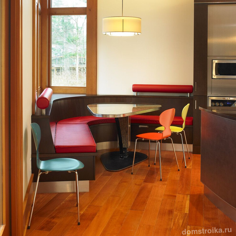 Полукруглый кухонный уголок с ярко дополненной спинкой, и легкие разноцветные стулья из металла и пластика, подходящие к динамичному современному оформлению всего помещения