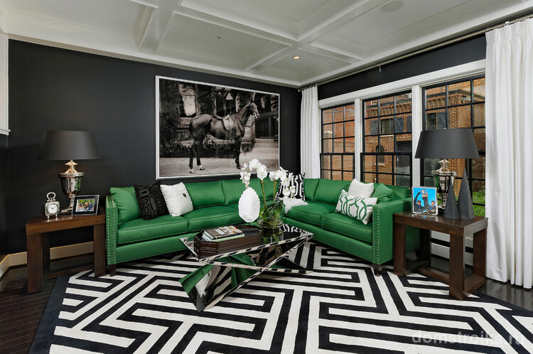 Черные стены, контрастные узоры ковра и большой угловой зеленый диван