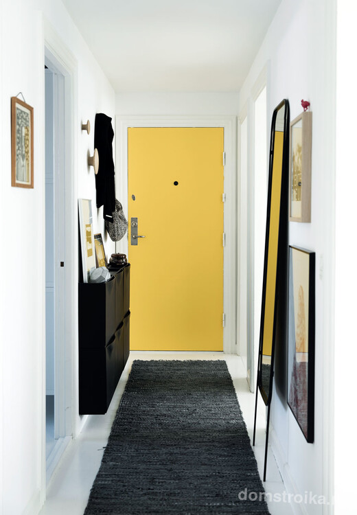 Узкий коридор с теплым акцентом на желтых входных дверях, высокое зеркало визуально увеличивает пространство, а маленькая навесная тумба практично вмещает обувь и все необходимые вещи