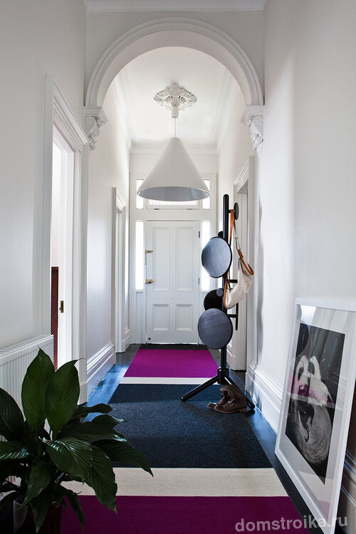 Стильный белый коридор частного дома с лаконичной люстрой и напольной вешалкой