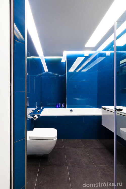 Смелое и очень красочное решение: расширяющий пространство синий глянец плитки и холодное освещение в небольшом совмещенном санузле