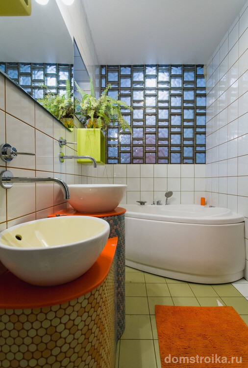 Современная небольшая ванная, где декором над угловой акриловой купелью служит светопропускающая перегородка из стеклоблоков
