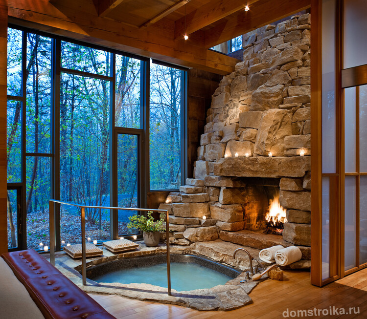 Шикарная встроенная ванна под стеклянной стеной, открывающей лесной вид. В такой комфортно в любое время года из-за камина с живым огнем рядом