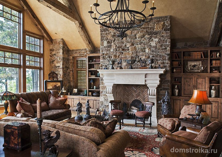 Каменные стены, темные массивные диваны, кованные предметы интерьера в гостиной домика-шале