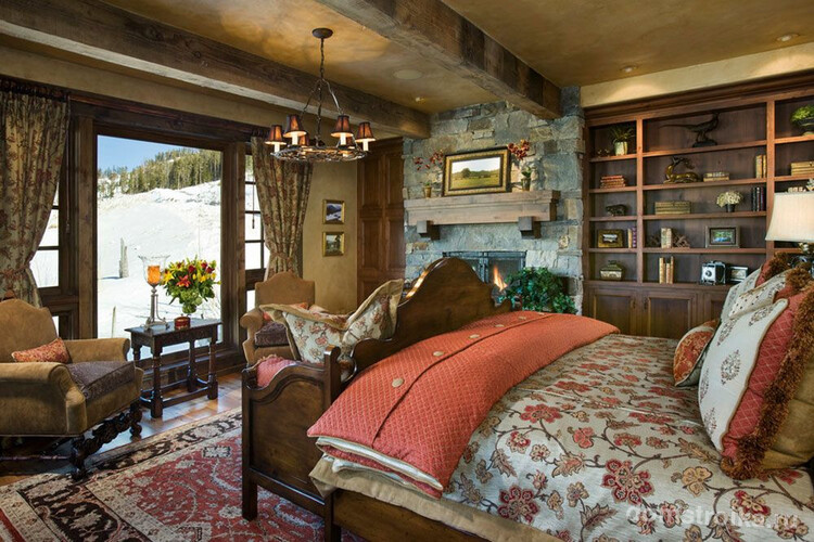 Оформление спальни в загородном доме: каменные стены, ковер на полу, натуральная постель, люстры, картины природы