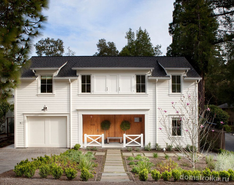 Белый двухэтажный дом, оформленный деревянным сайдингом, со встроенным гаражом