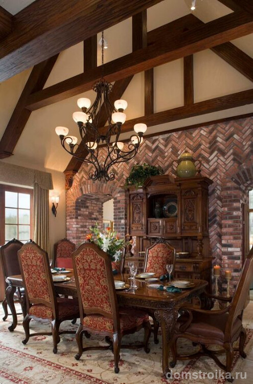 Обеденная комната в готическом стиле: потолок с деревянными балками, декоративный кирпич на стенах, большие окна и стилизованная мебель