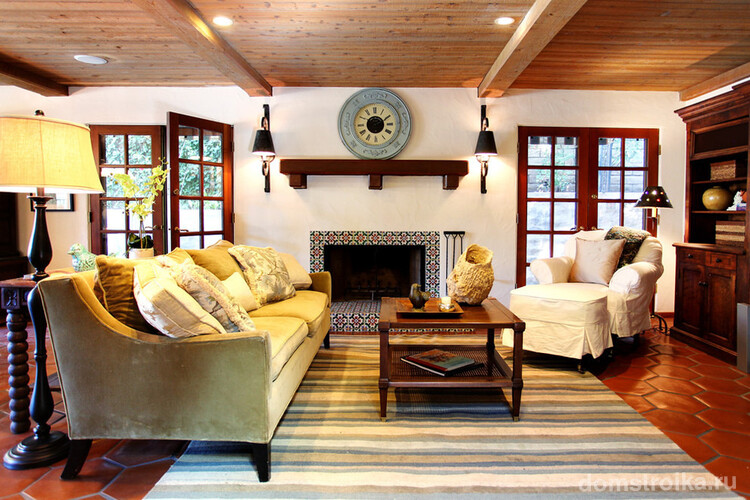Деревянные балки на потолке, большие окна, ковер с восточными элементами в интерьере гостиной