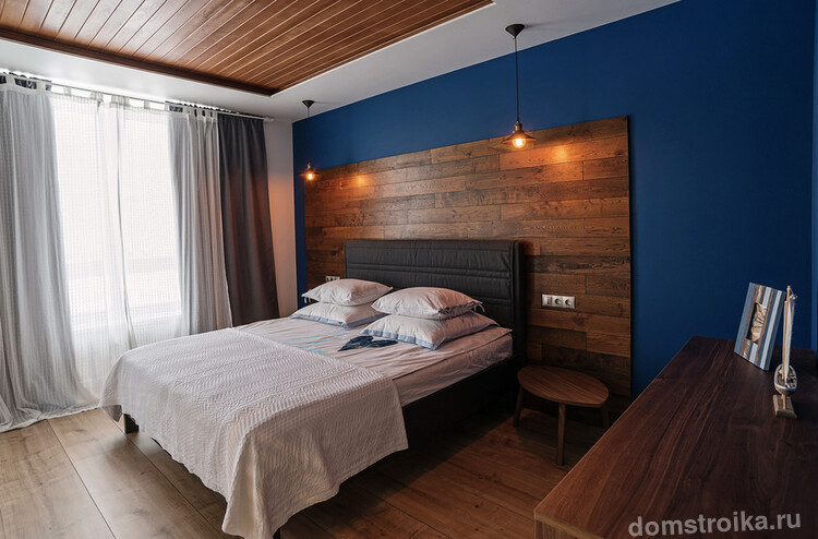 Стильная спальня с темно-синей стенкой и деревянным изголовьем кровати