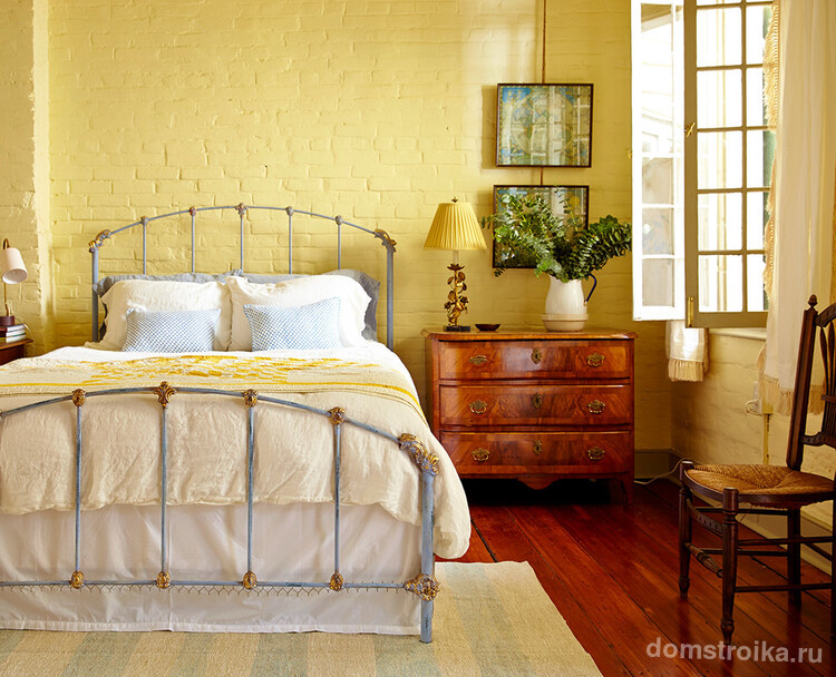 Великолепное сочетание кованной кровати и кирпичной кладки, окрашенной в желтый цвет, в интерьере спальни