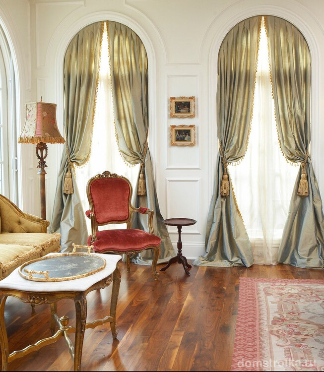 Роскошная гостиная комната в классическом стиле. Гибкий карниз для штор, подвязанных кисточками, на арочном окне – особенность интерьера
